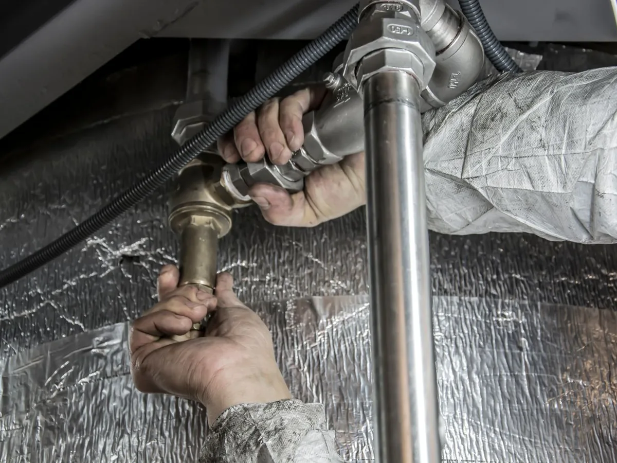 Copperline technician clearing a clogged drain line under a kitchen sink